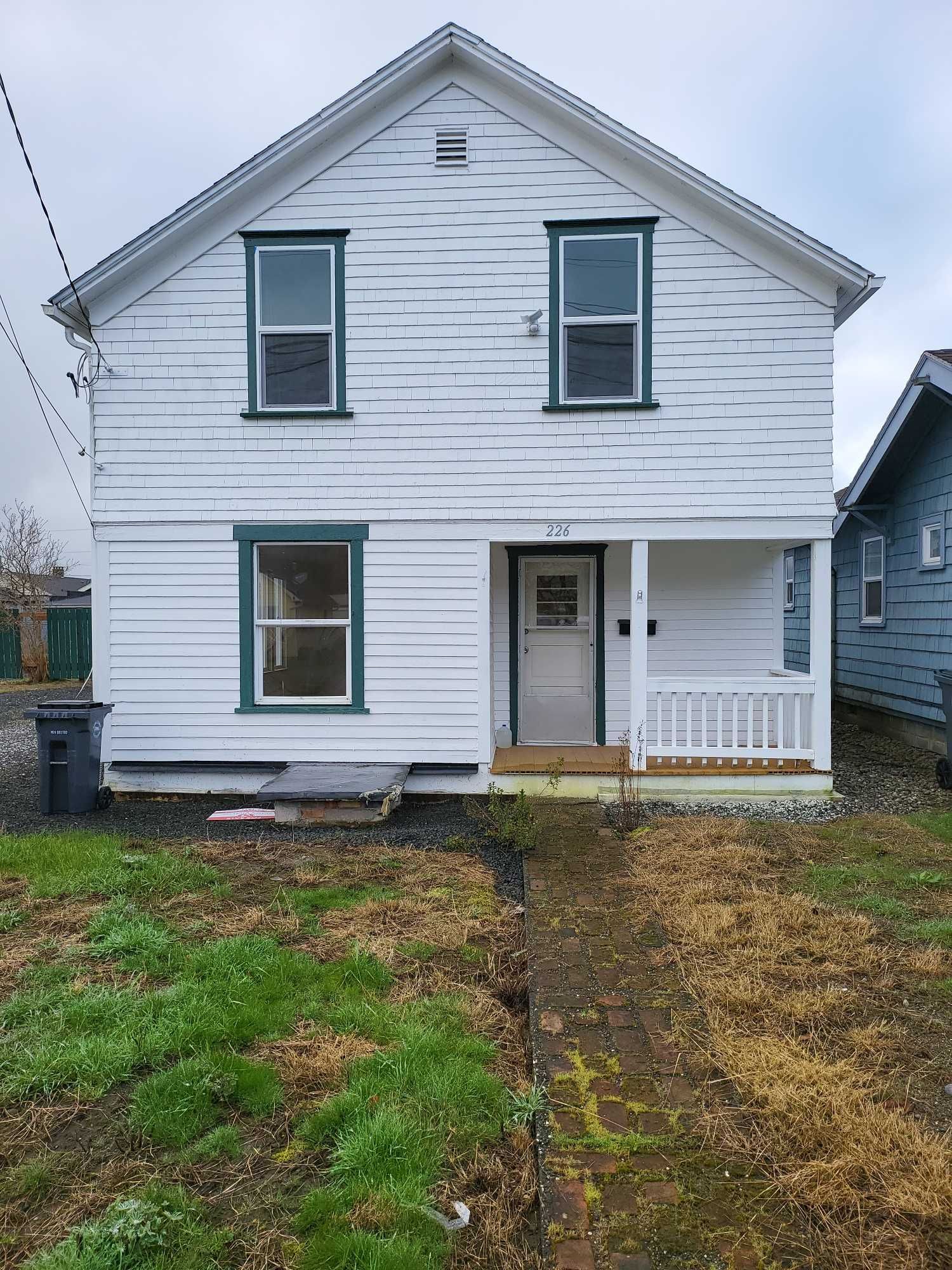 A white house with green trim is sitting in the middle of a grassy field.