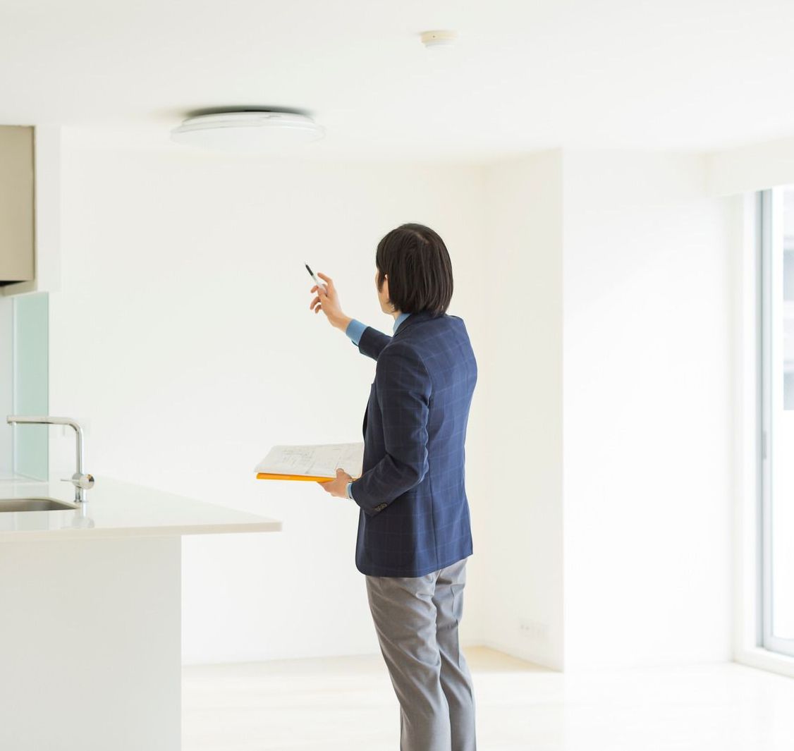 A man in a blue jacket is standing in a kitchen holding a clipboard.