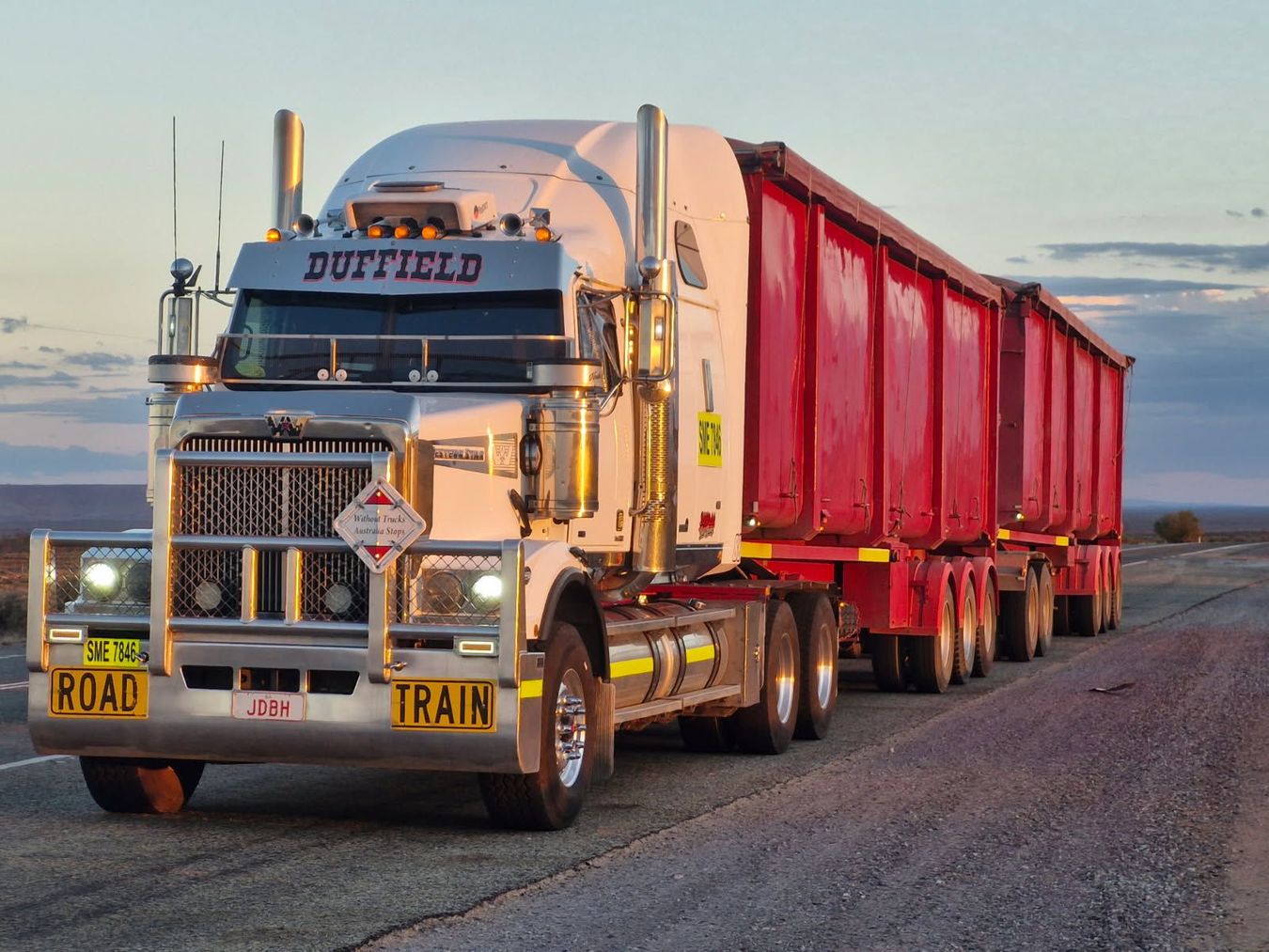 White semi-trucks parked in a row on pavement under a cloudy sky.