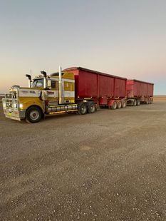 A semi-truck with a covered trailer traveling on an empty highway, next to a grassy hill.
