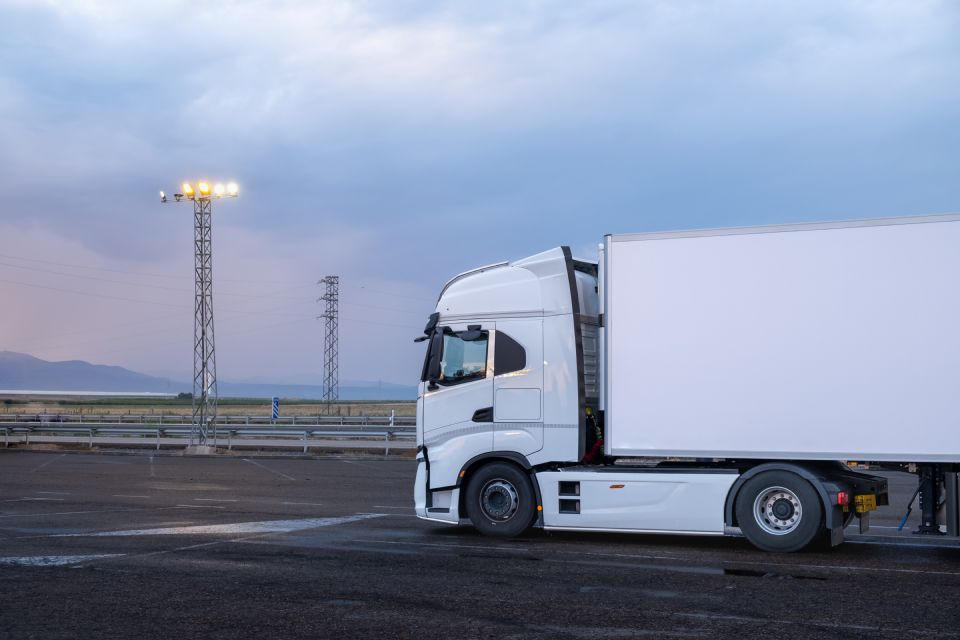 White semi-truck parked outdoors at dusk, with cloudy sky and utility towers.
