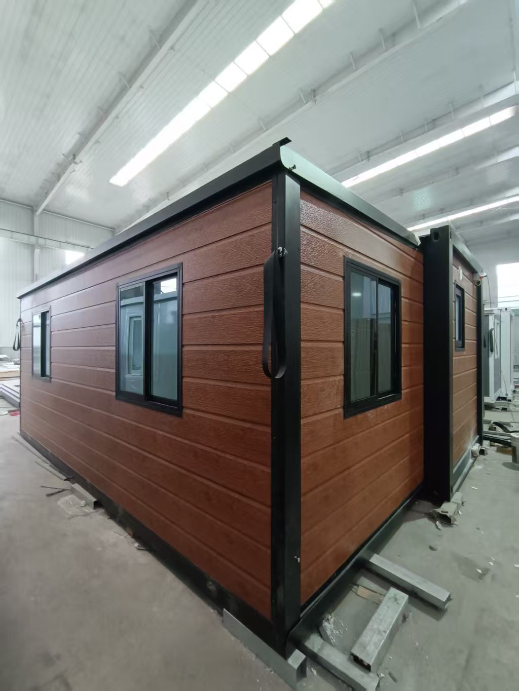 Prefabricated modular home with wood-look siding, white trim, and glass doors and windows inside a warehouse. — Expandable Housing in Inala, QLD