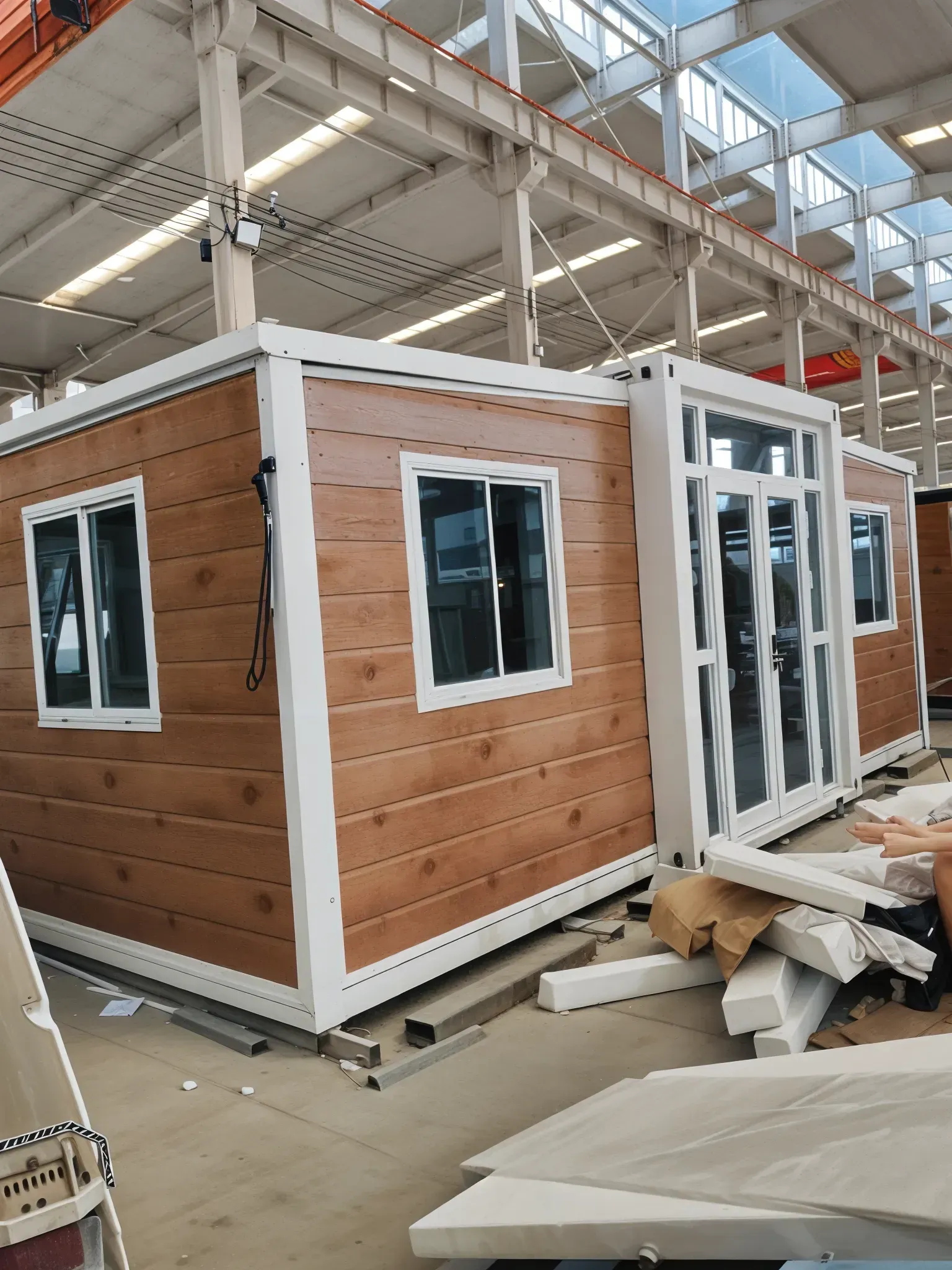 Prefabricated modular home with wood-look siding, white trim, and glass doors and windows inside a warehouse. — Expandable Housing in Inala, QLD
