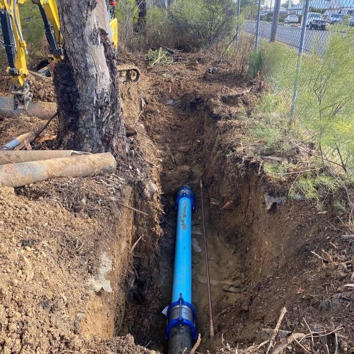 A Blue Water Pipe Installed in a Trench Beside a Fence and Trees — Huddo's Plumbing Service in Port Stephens, NSW