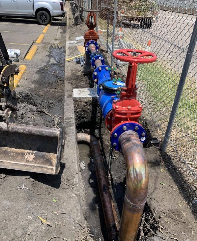 Blue and Red Water Valves Installed in a Trench Alongside a Chain-link Fence — Huddo's Plumbing Service in Wallalong, NSW