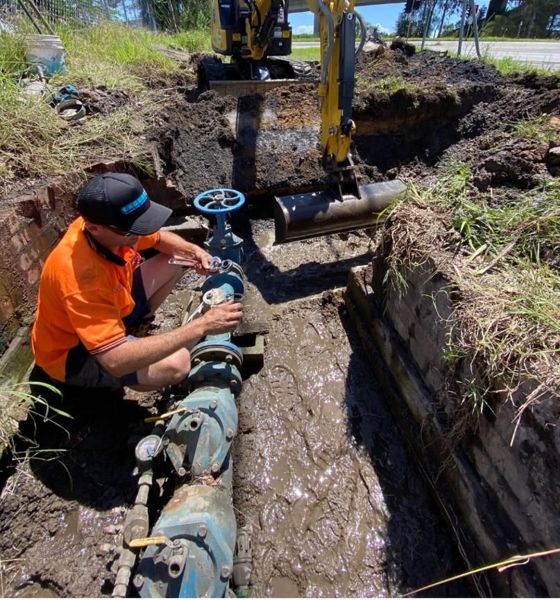 Construction Worker Adjusts Valve in a Muddy Trench — Huddo's Plumbing Service in Wallalong, NSW