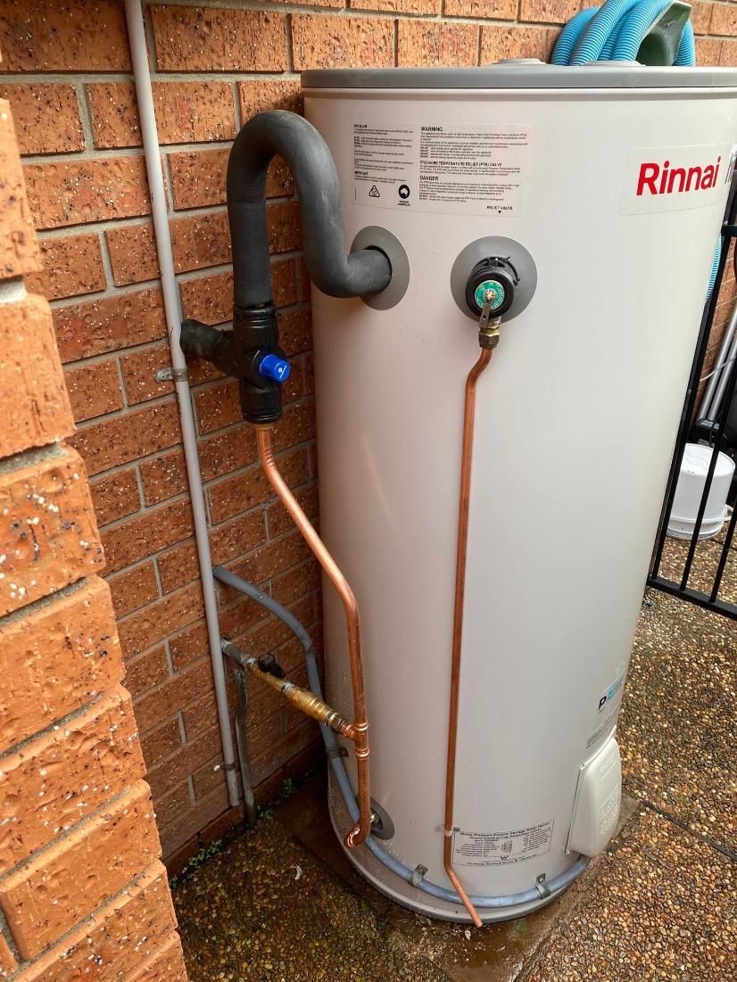 Rinnai Hot Water Heater Against a Brick Wall, With Copper Pipes and Black Valve — Huddo's Plumbing Service in Wallalong, NSW