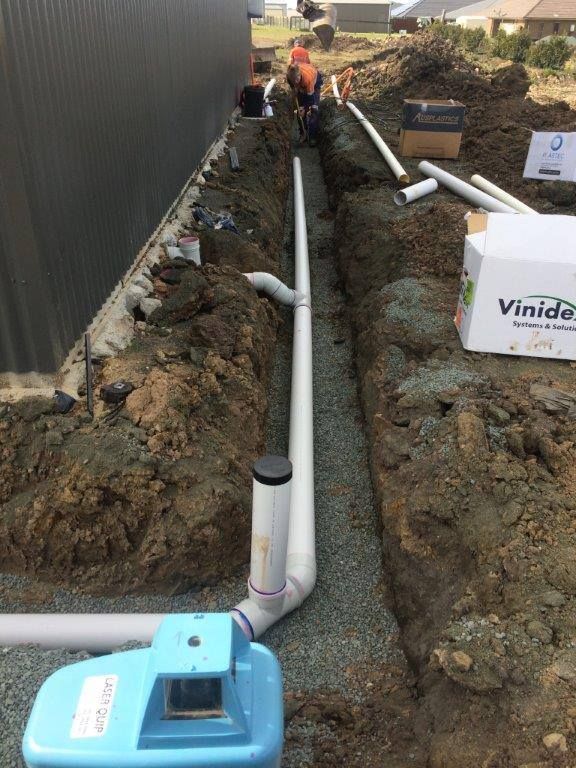 Construction Workers Installing Pipes in a Trench Next to a Building — Huddo's Plumbing Service in Wallalong, NSW