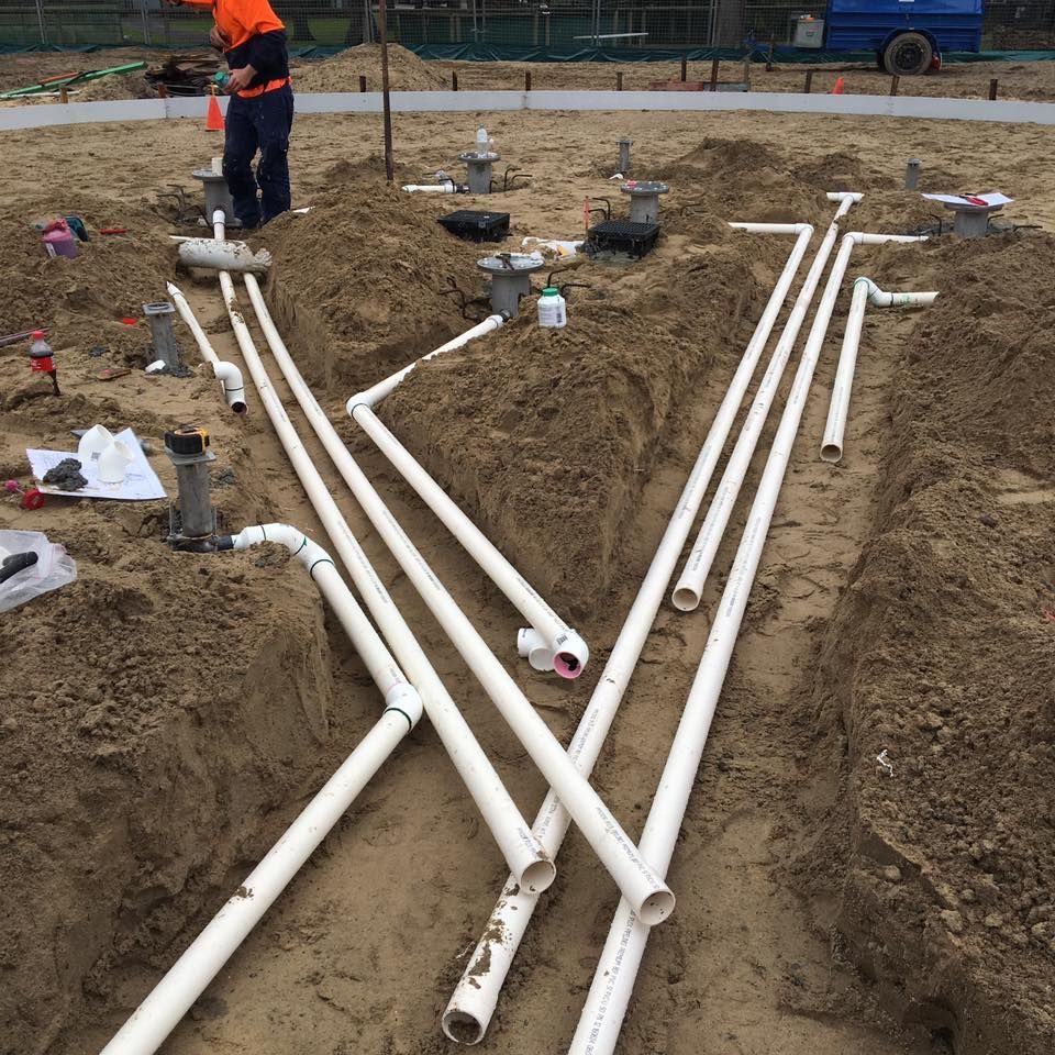 Worker Installing White Pvc Pipes in Trenches in the Dirt — Huddo's Plumbing Service in Wallalong, NSW