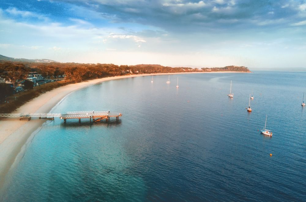 Beach Scene With Sandy Shore, Pier, and Boats — Huddo's Plumbing Service in Port Stephens, NSW