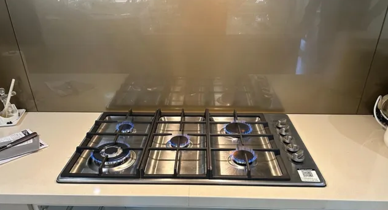 Gas Stovetop With Blue Flames on a Countertop Above Open Cabinet With Dishware — Huddo's Plumbing Service in Wallalong, NSW