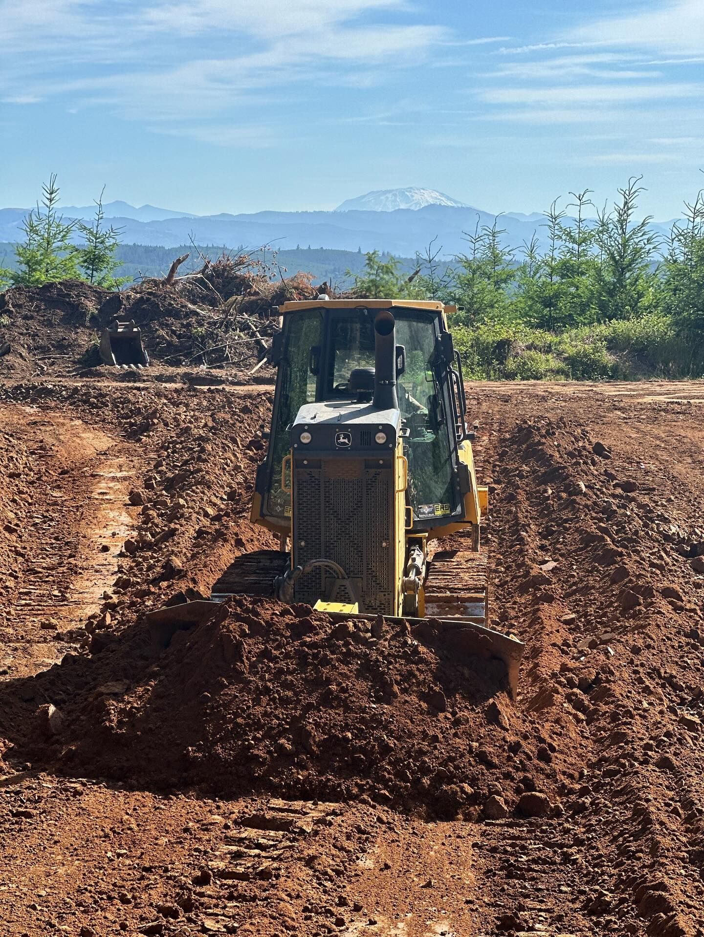 Yellow bulldozer pushing dirt on a muddy construction site with mountains in the background