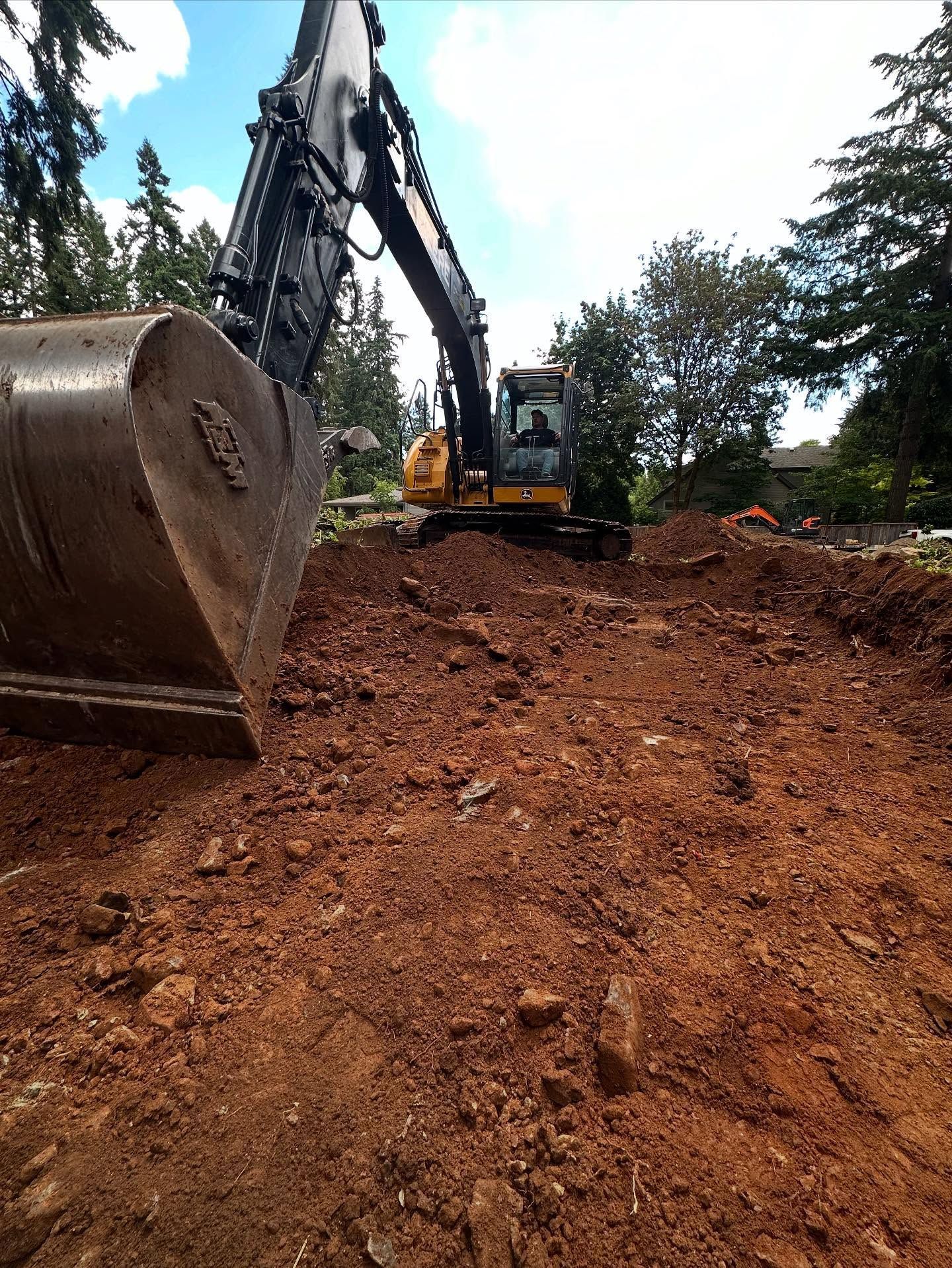 Excavator with raised bucket working on a muddy construction site under a partly cloudy sky