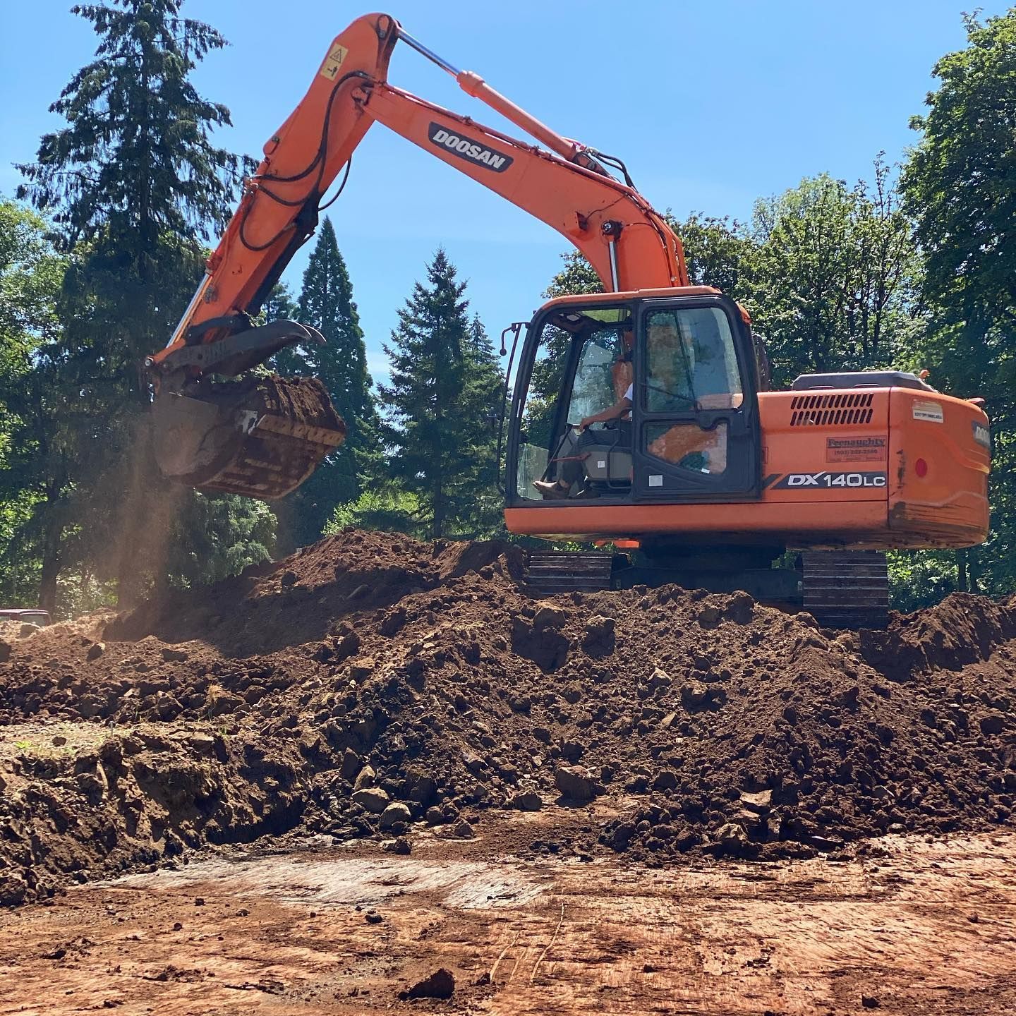 Orange excavator dumping dirt on a mound at a construction site under a blue sky.
