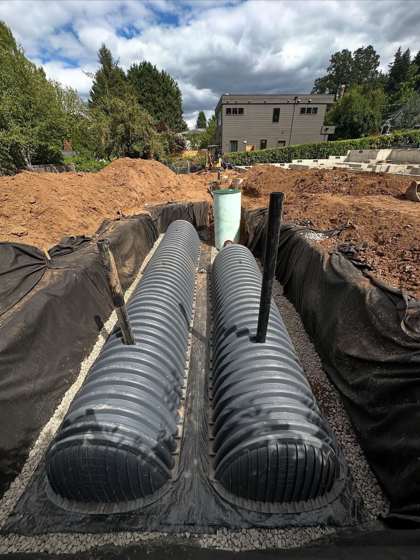 Two black corrugated drainage pipes installed in a gravel trench at a construction site.