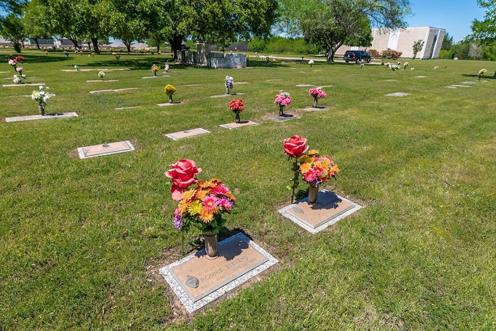 A cemetery filled with graves and flowers on a sunny day.