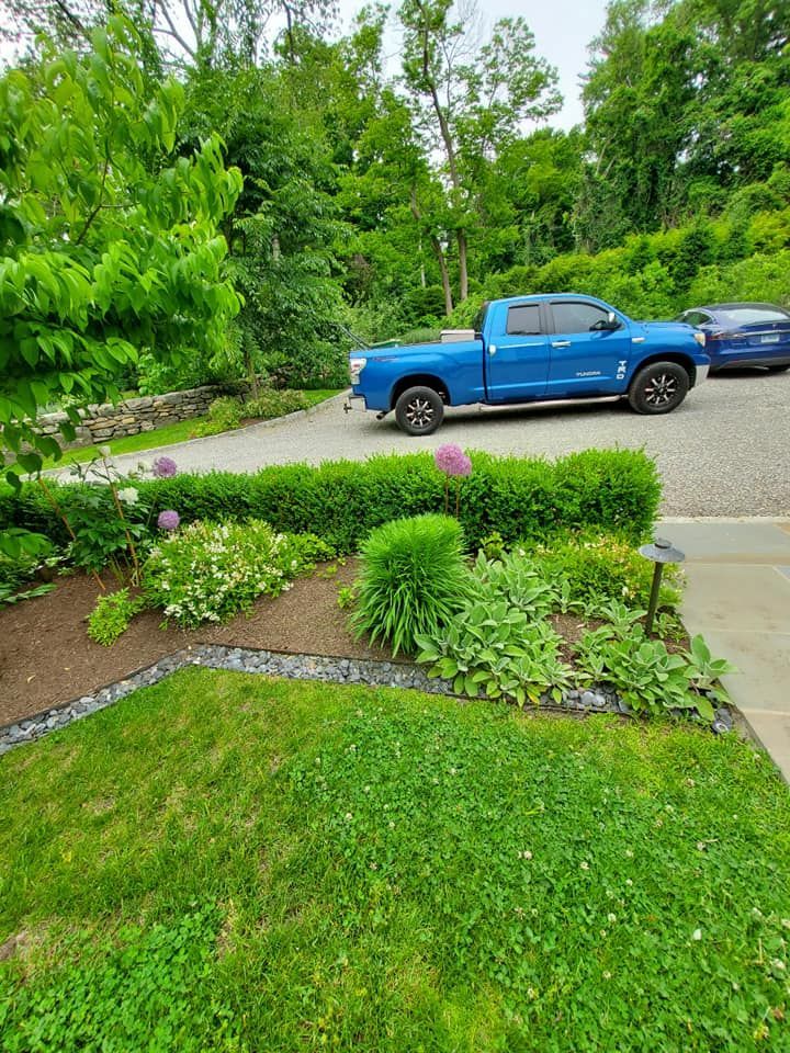 A blue truck is parked in a driveway next to a lush green yard.