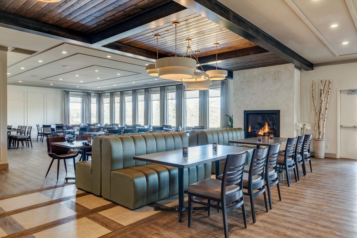 A dining area with green booths, tables, chairs, pendant lights, and a stone fireplace.
