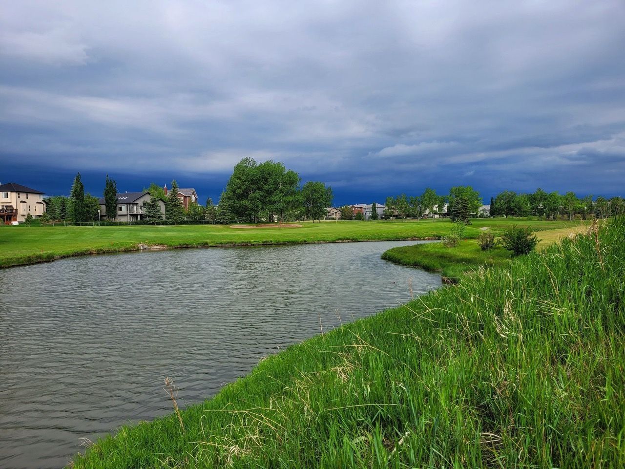 An aerial view of a golf course with golf carts lined up, near a clubhouse, with trees and a cloudy sky.