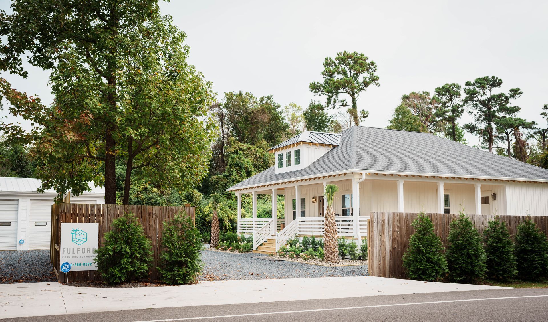 A white house with a gray roof is surrounded by trees