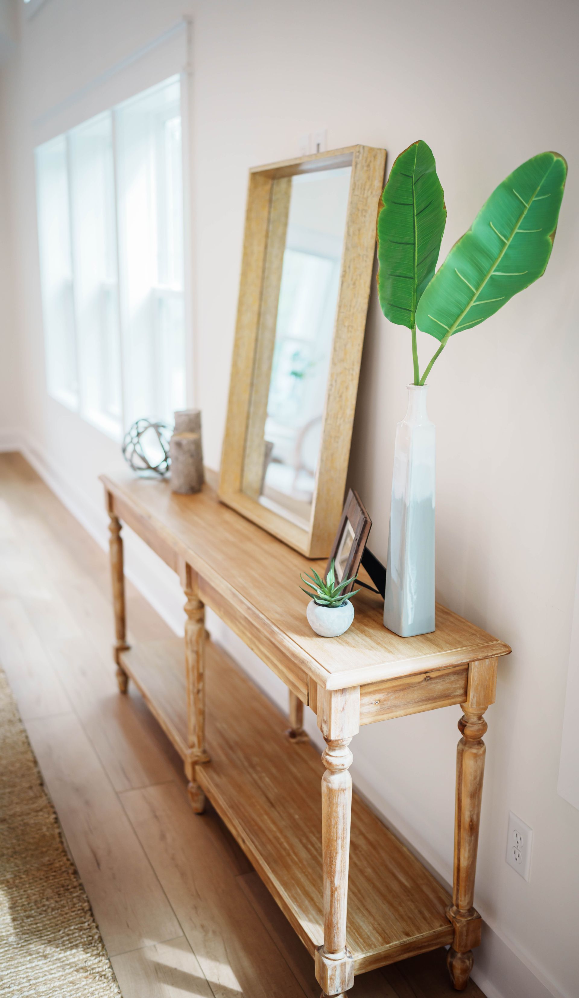 A wooden table with a mirror and a plant on it in a hallway.