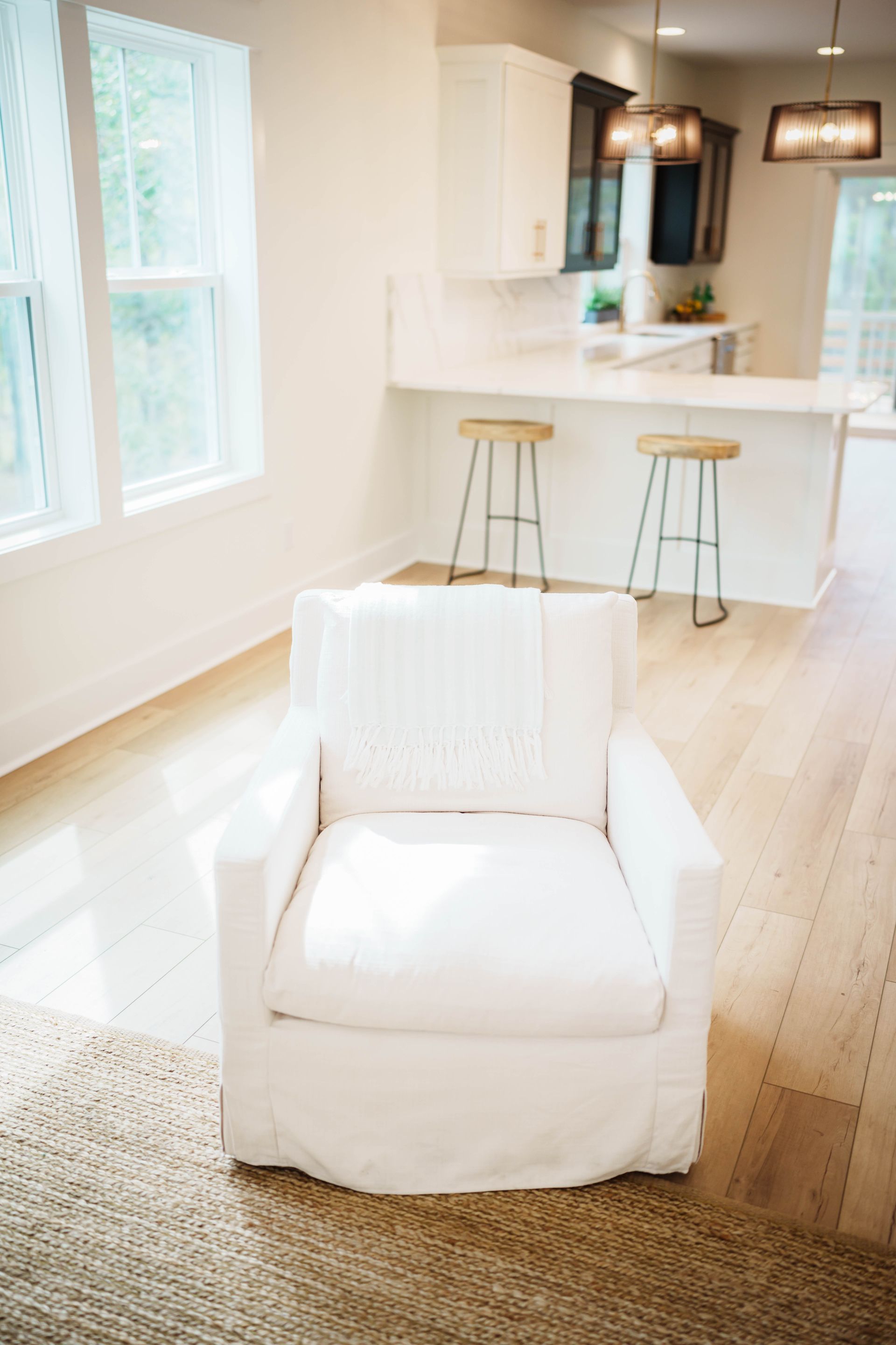 A white chair is sitting in a living room in front of a kitchen.