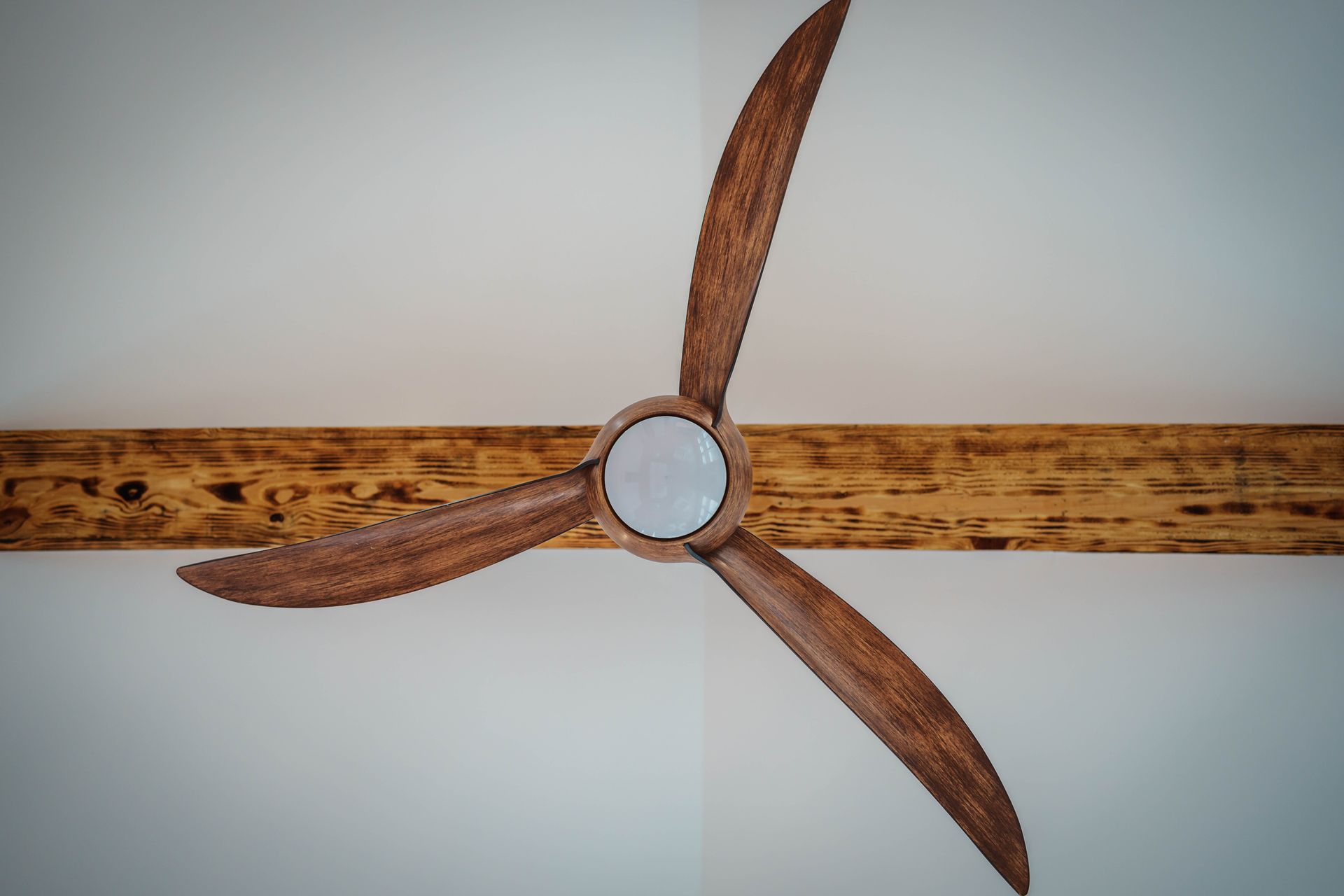 A wooden ceiling fan with three blades on a white wall