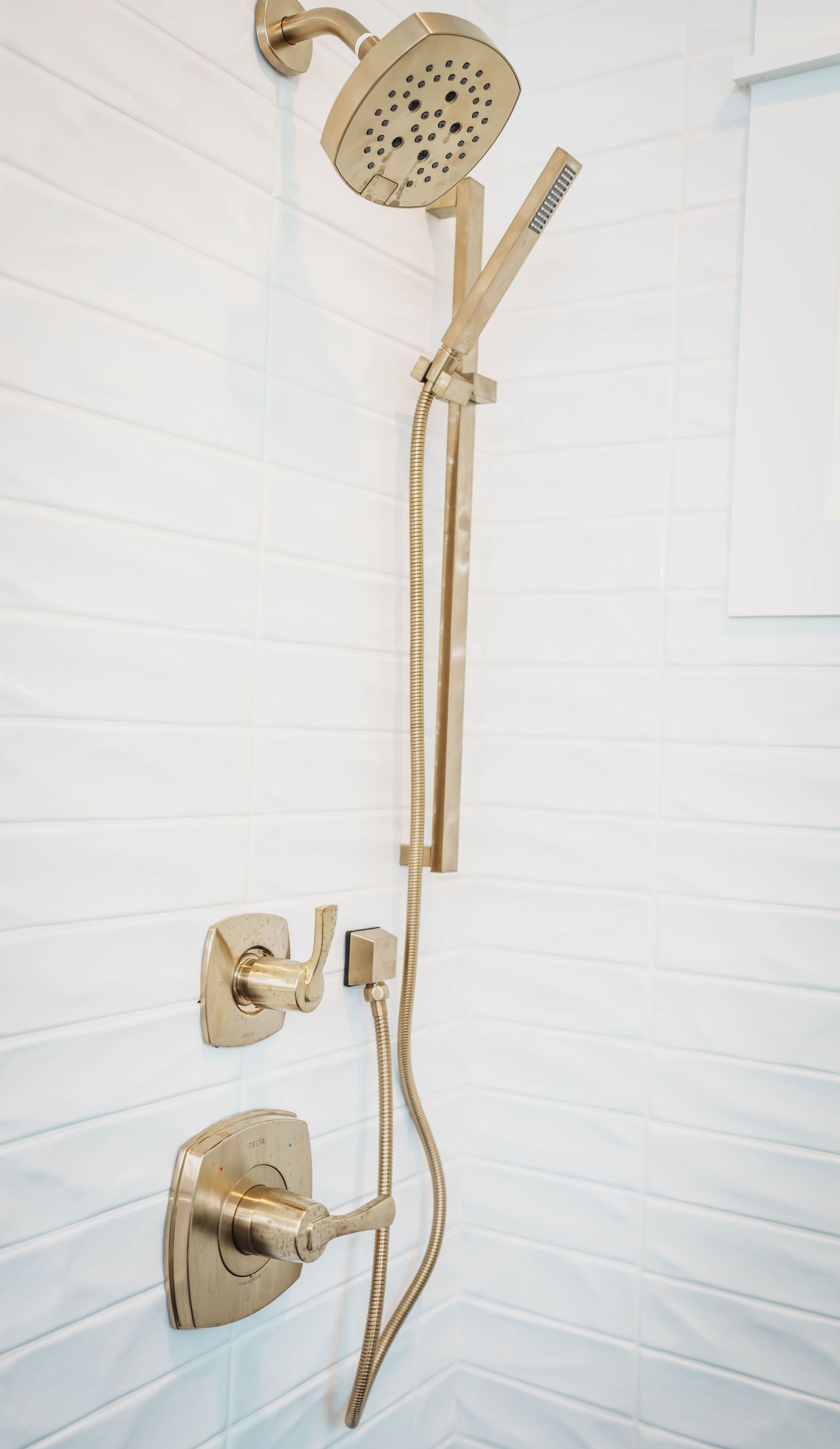 A gold shower head is mounted on a white tiled wall.