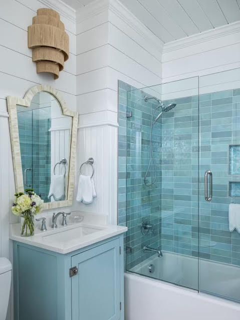 A bathroom with blue tiles , a sink , a mirror and a bathtub.