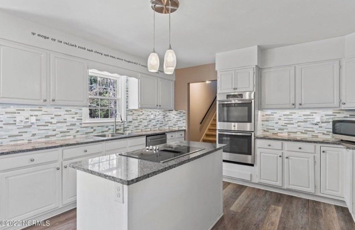 A kitchen with white cabinets , granite counter tops , stainless steel appliances and a large island.