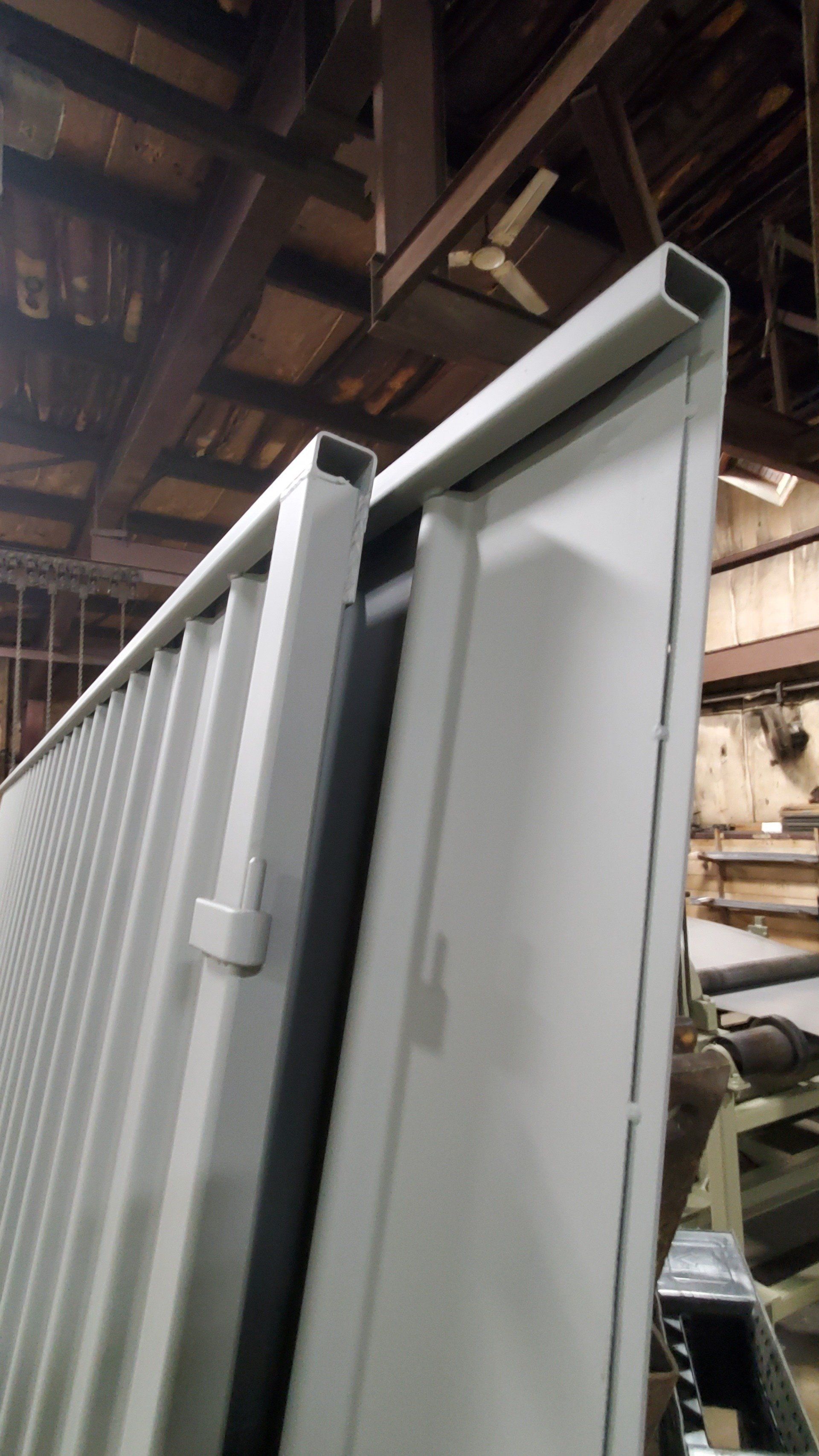 A white fence is sitting in a warehouse under a ceiling fan.