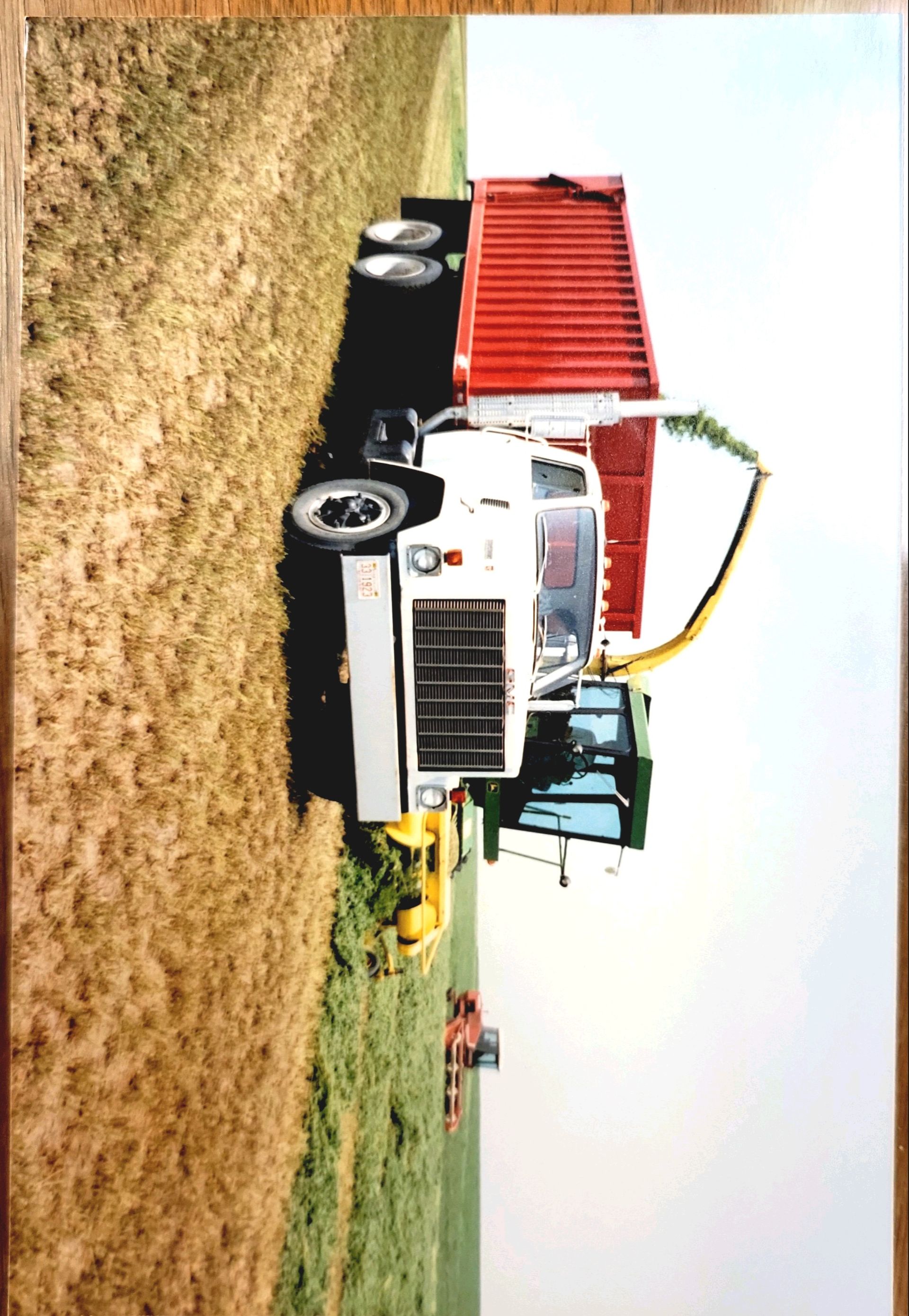 A white truck with a red dumpster on the back is in a field