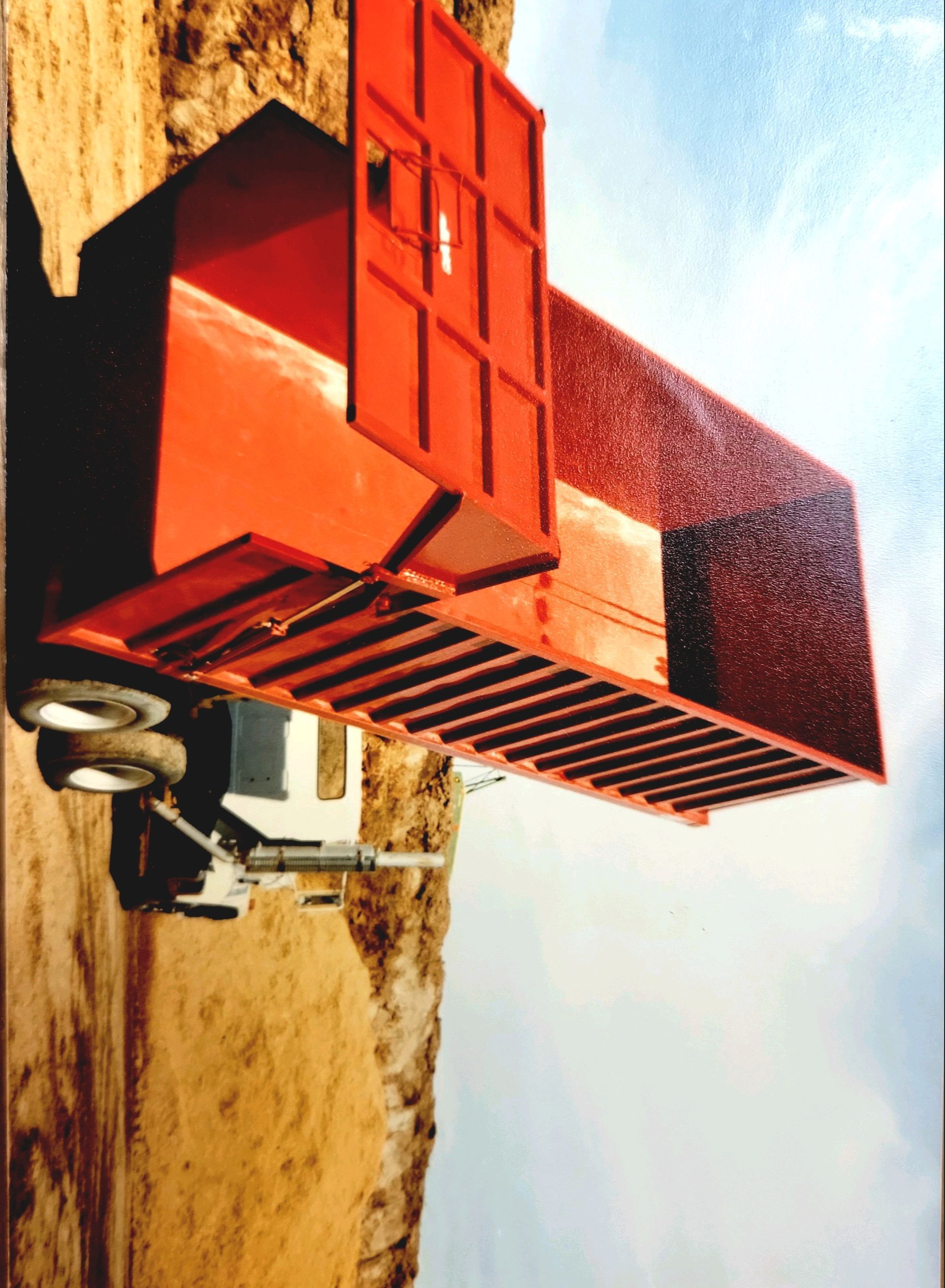 A red dump truck is parked on a dirt road