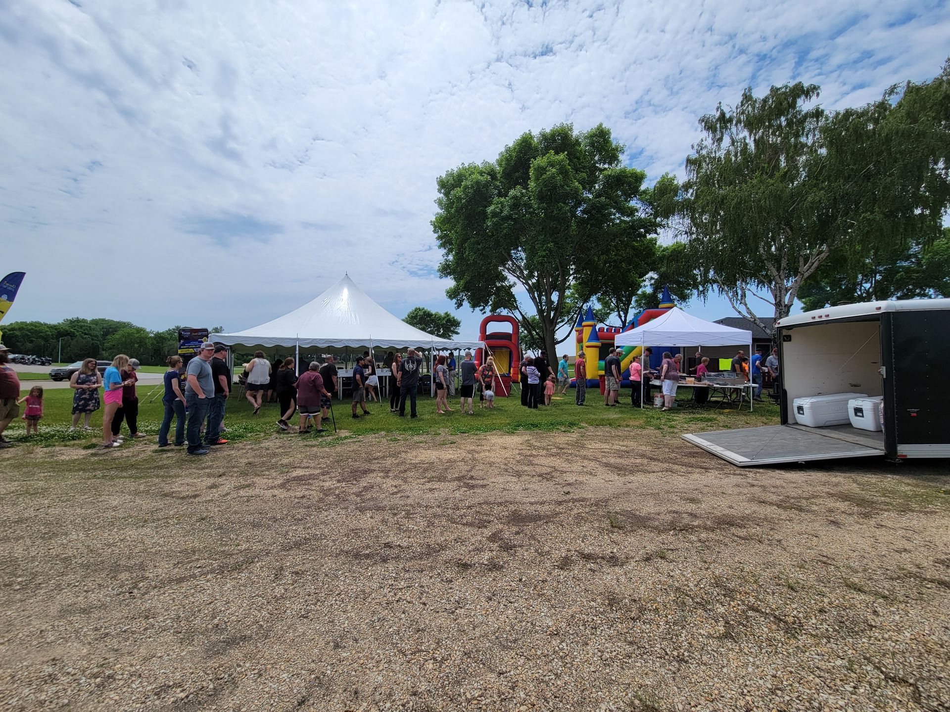 A group of people are standing in a field with tents and a trailer.