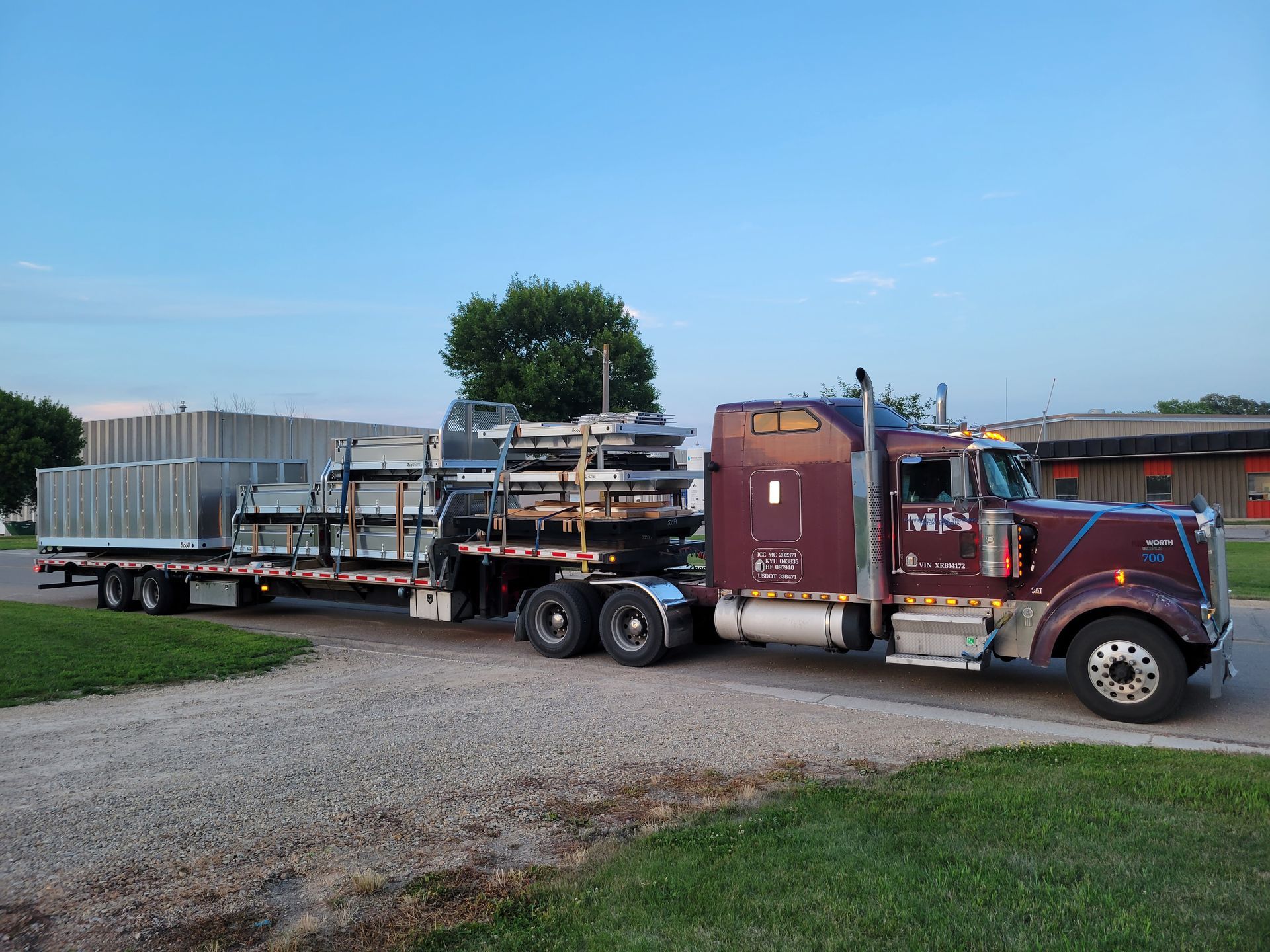 A semi truck is driving down a gravel road carrying a flatbed trailer.