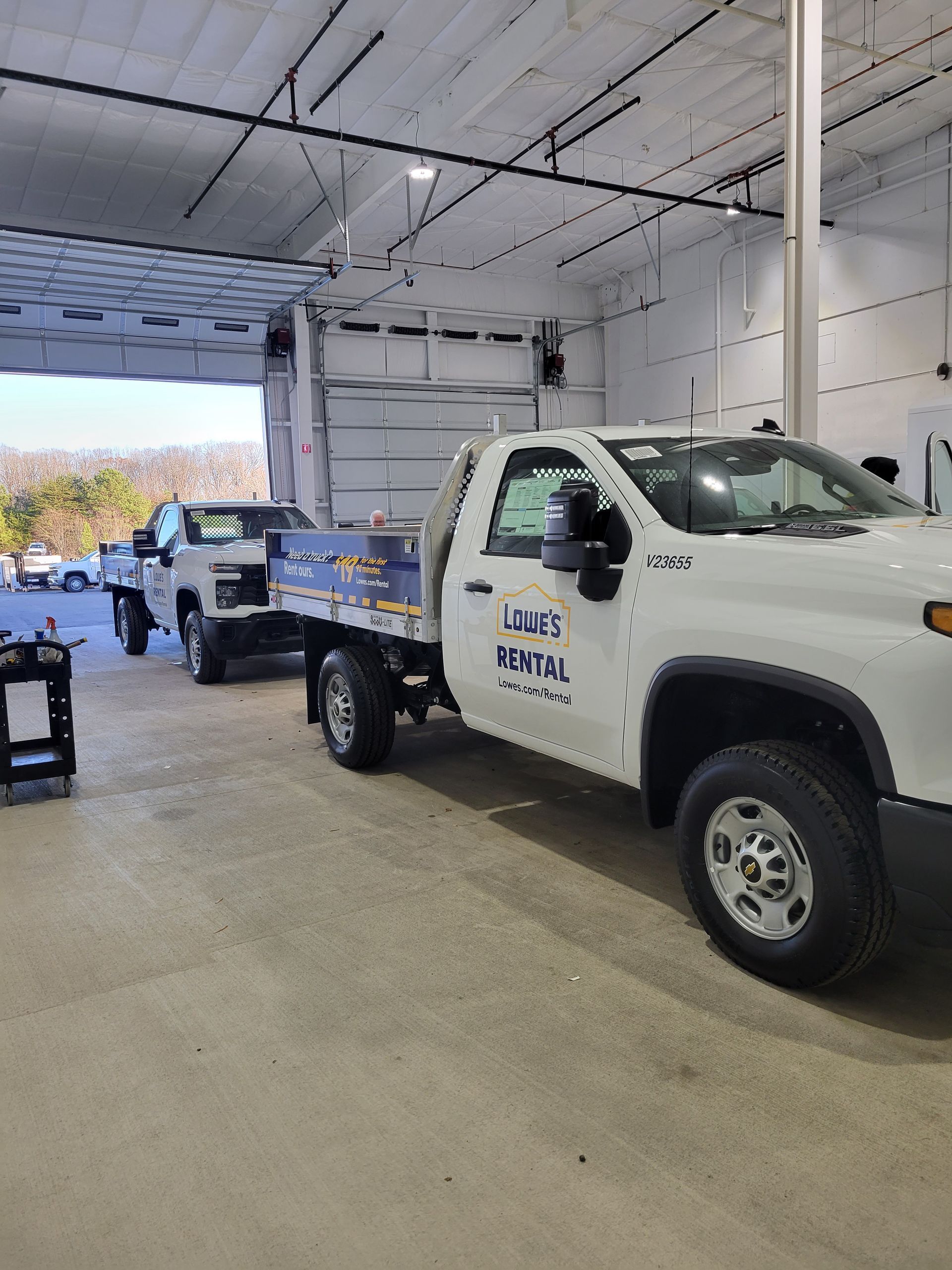 A white truck is parked in a garage next to another truck.