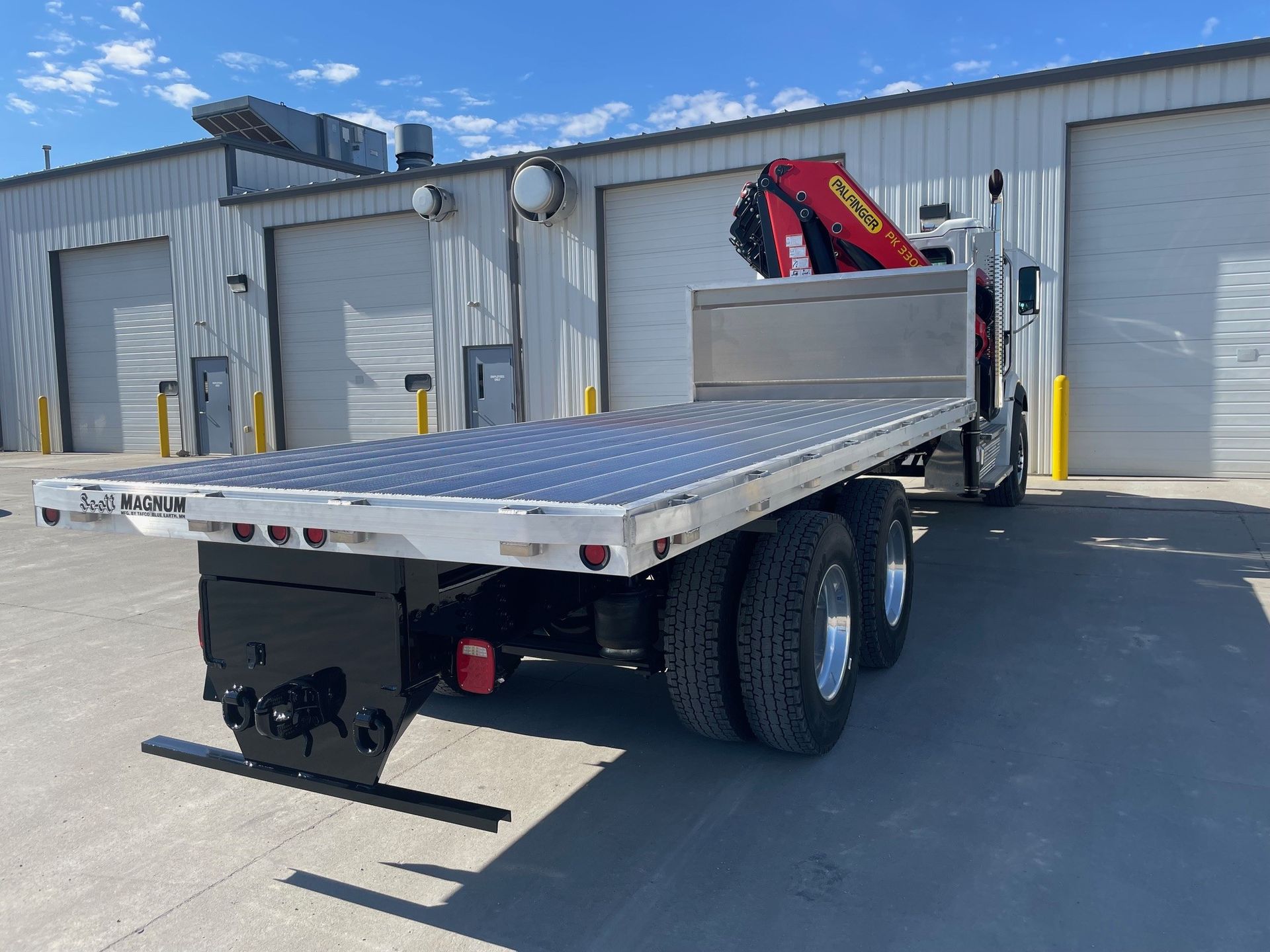 A flatbed truck with a crane on the back is parked in front of a building.
