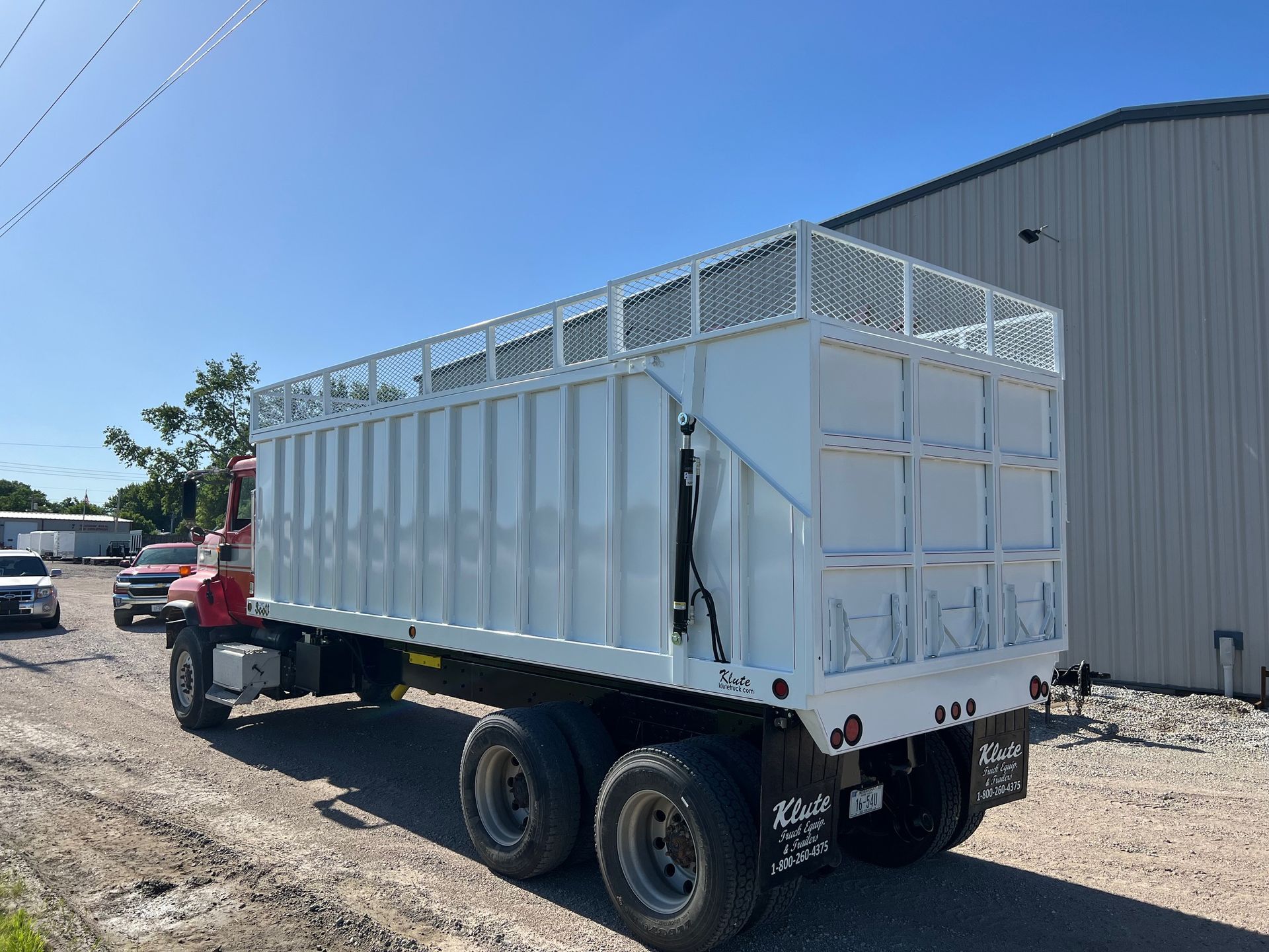 A white semi truck is parked on a dirt road in front of a building.