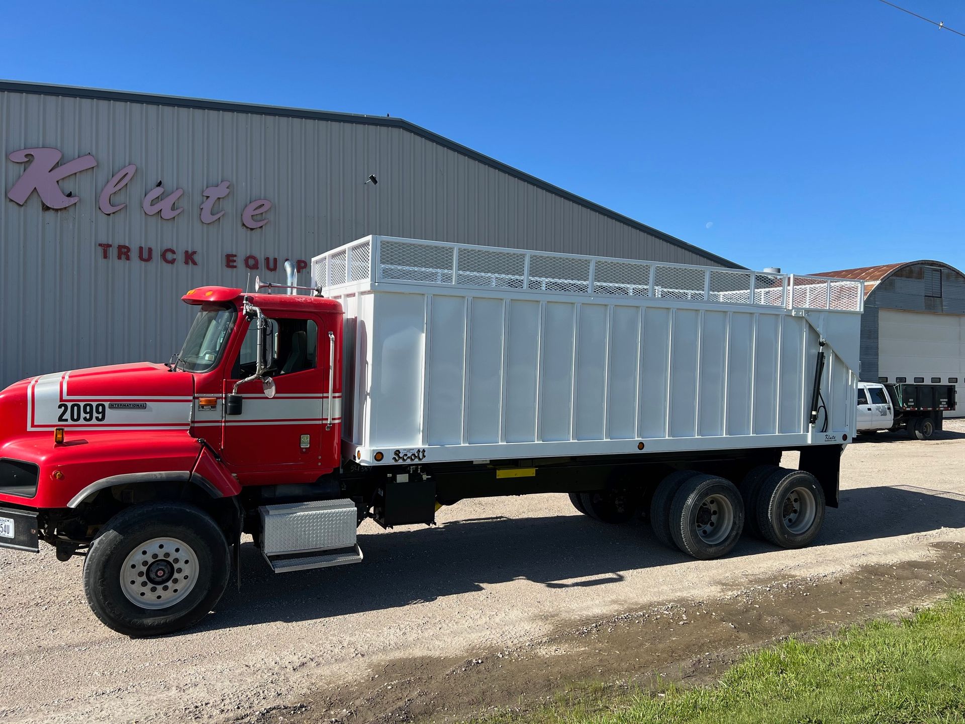 A red and white dump truck is parked in front of a building.