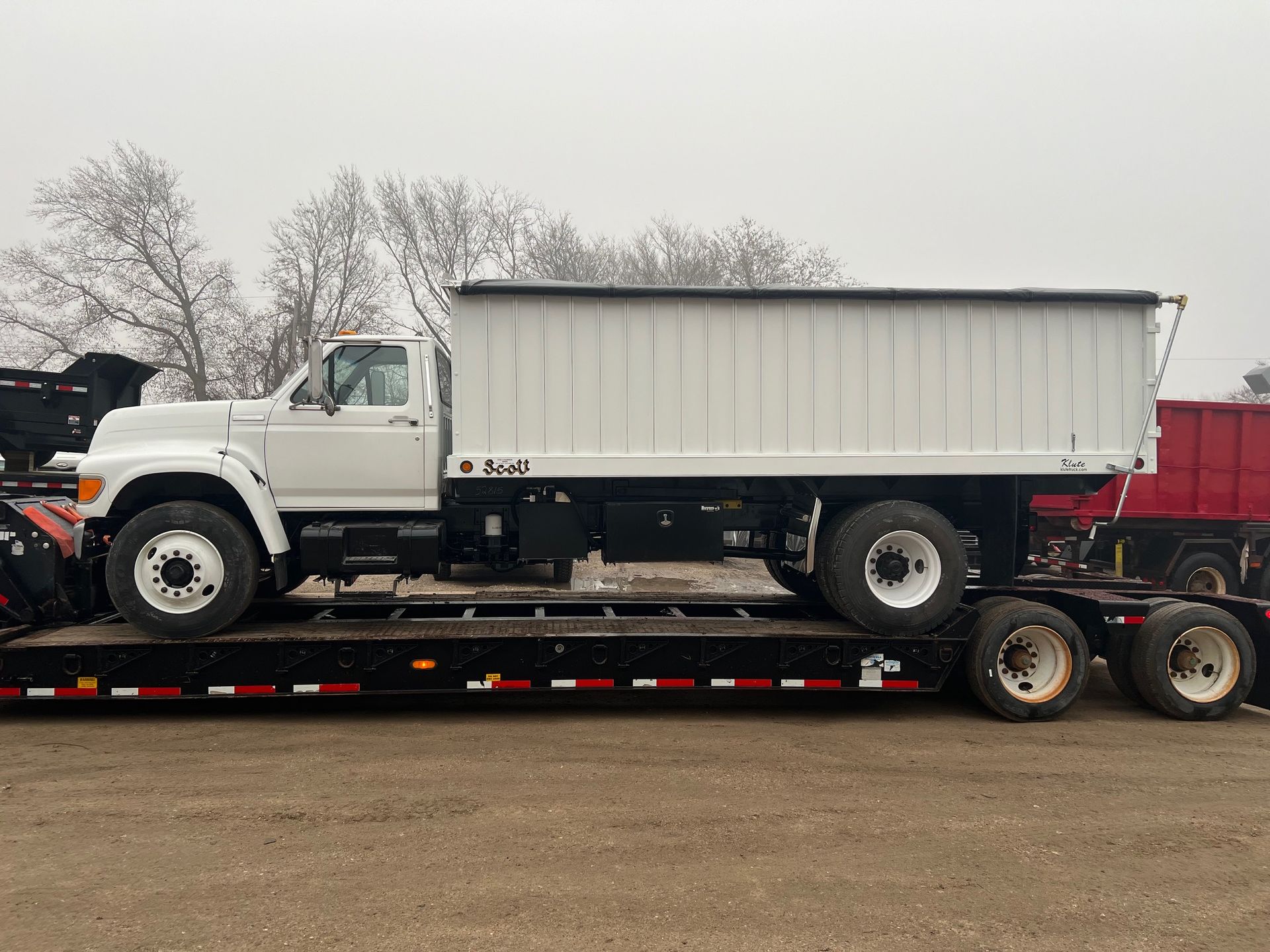 A white dump truck is sitting on top of a trailer.