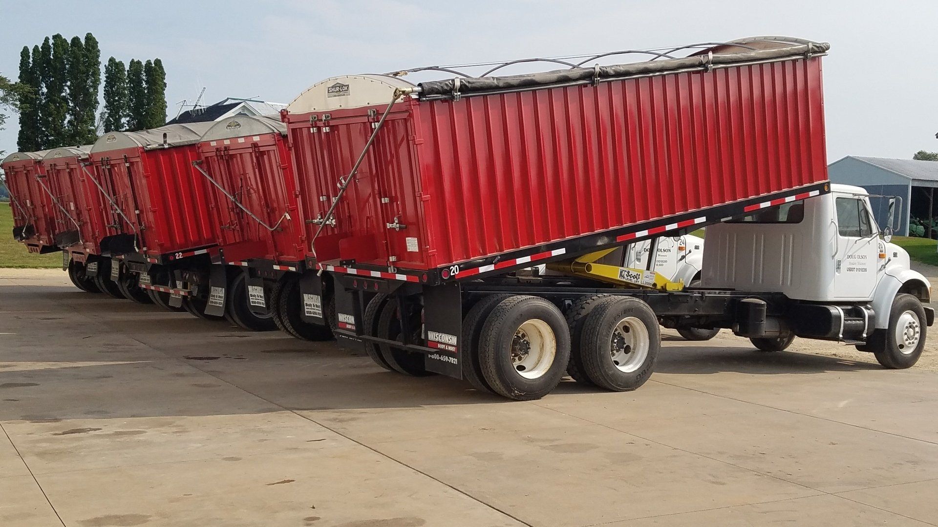 A row of red semi trucks are parked in a parking lot.
