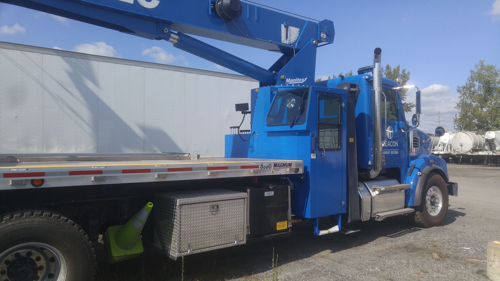A blue truck with a crane on the back is parked in a parking lot.