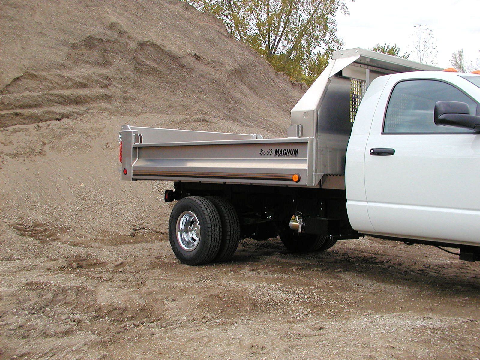 A white dump truck is parked in front of a pile of dirt