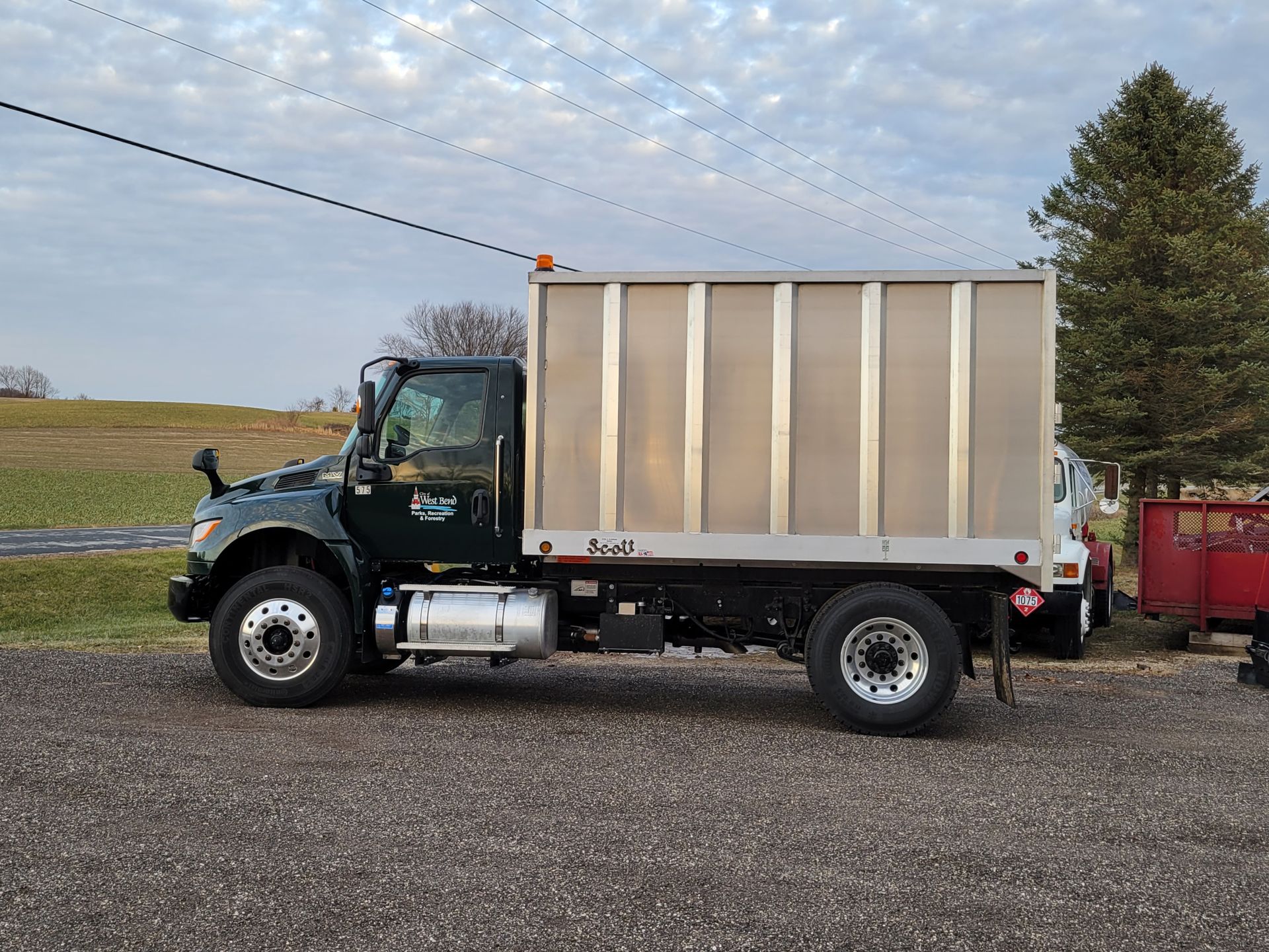 A truck with a box on the back is parked in a gravel lot.