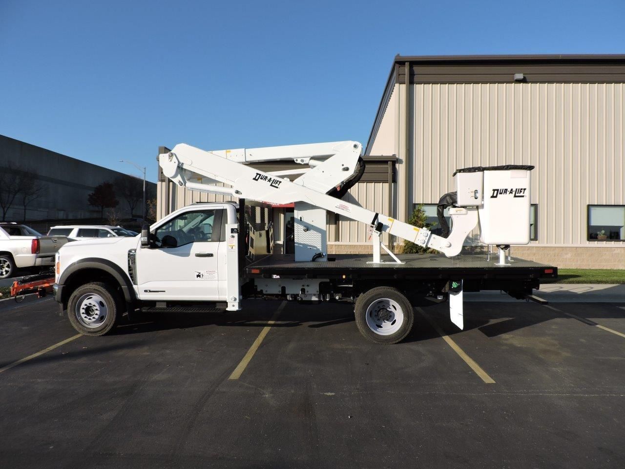 A white aerial lift truck is parked in a parking lot in front of a building.