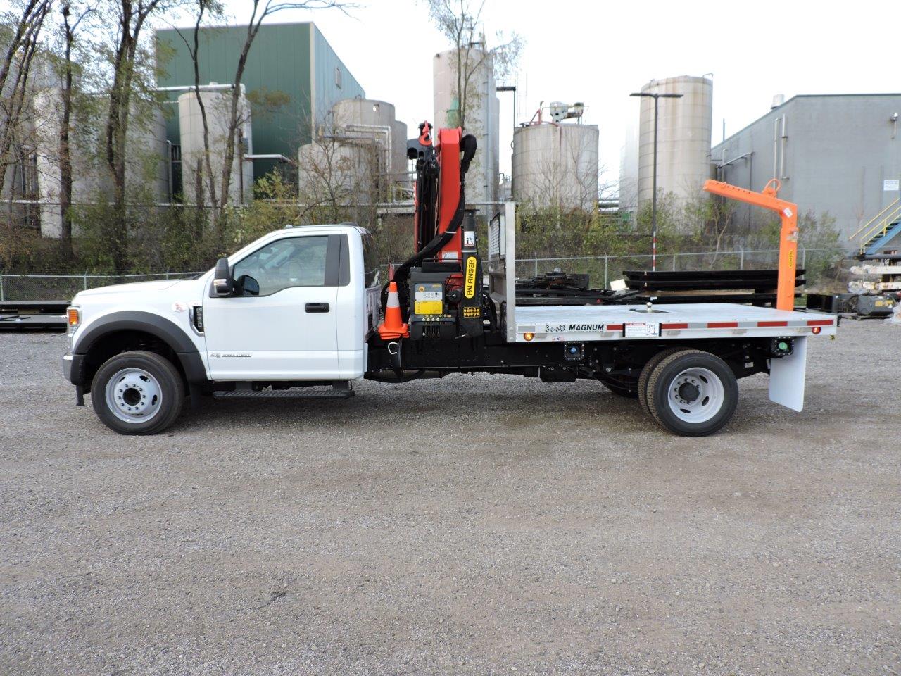 A white truck with a crane on the back is parked in a gravel lot.