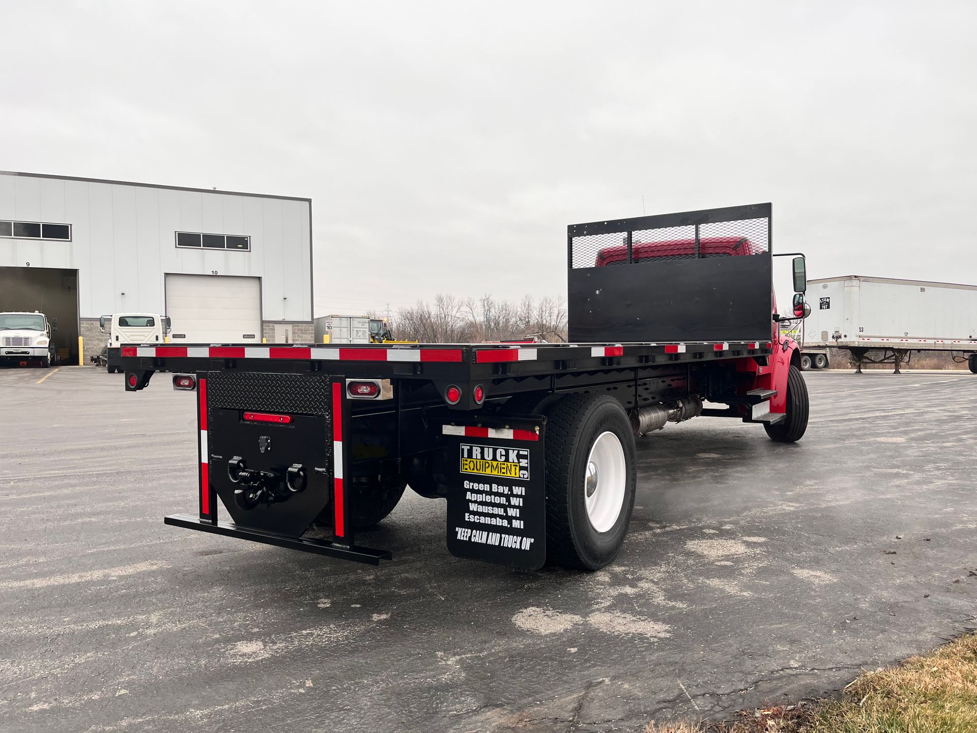 A flatbed truck is parked in a parking lot in front of a building.