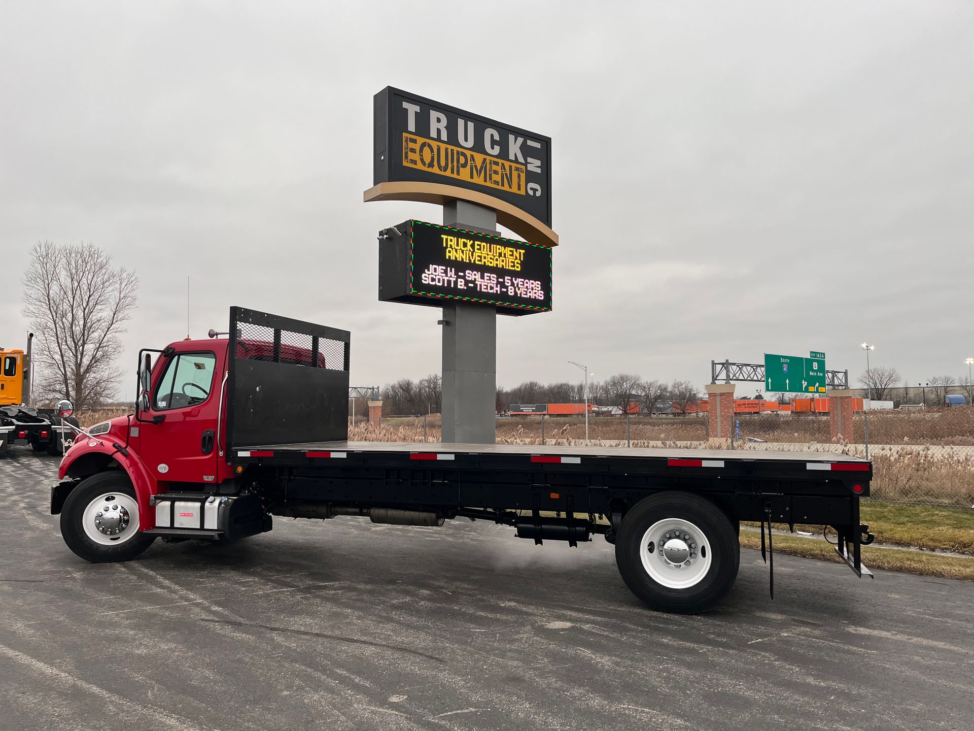 A red flatbed truck is parked in front of a truck equipment sign.