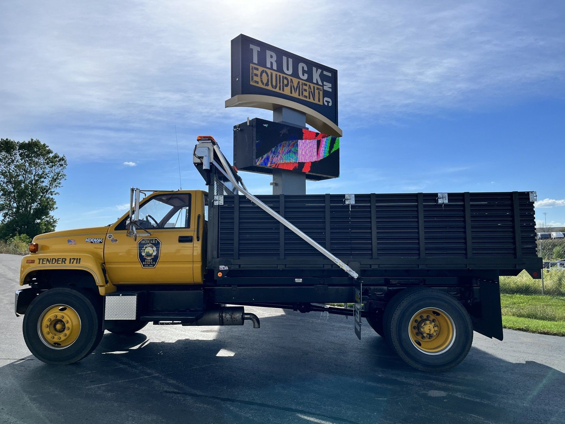 A yellow dump truck is parked in front of a truck equipment sign.