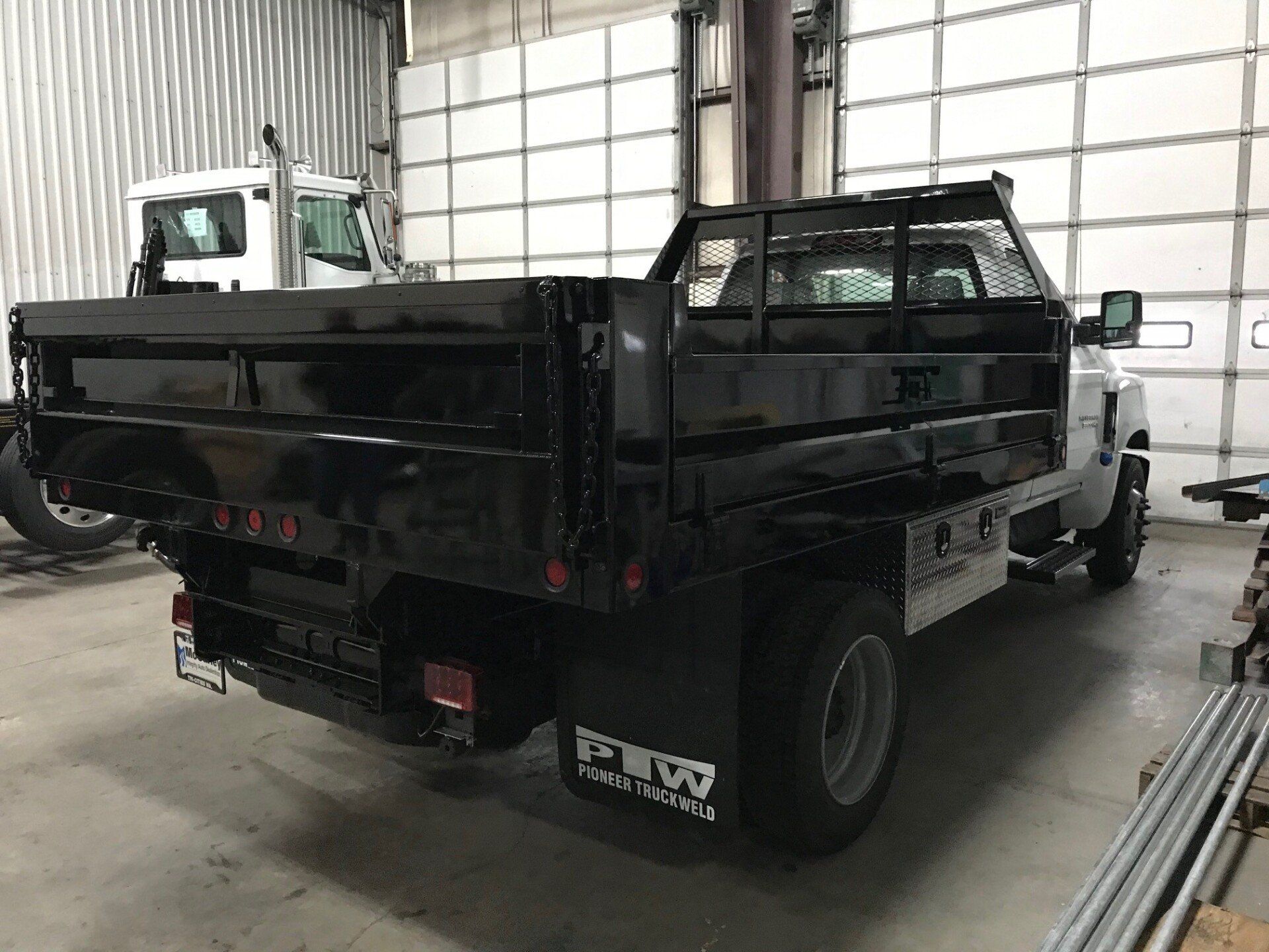 A black dump truck is parked in a garage next to a white truck.